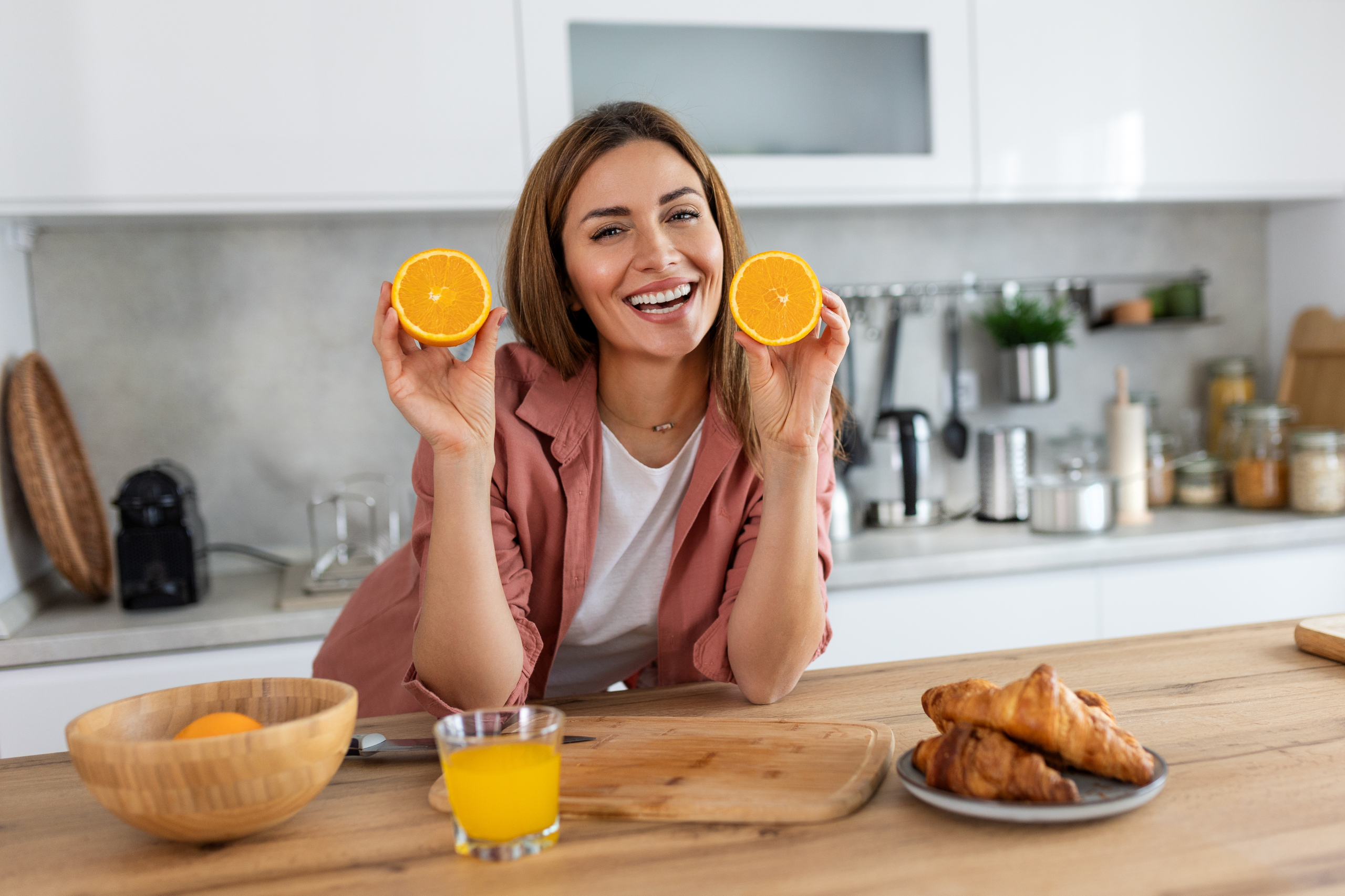 Beautiful young woman drinking fresh orange juice in kitchen. Healthy diet. Happy young woman with glass of juice and orange at table in kitchen.